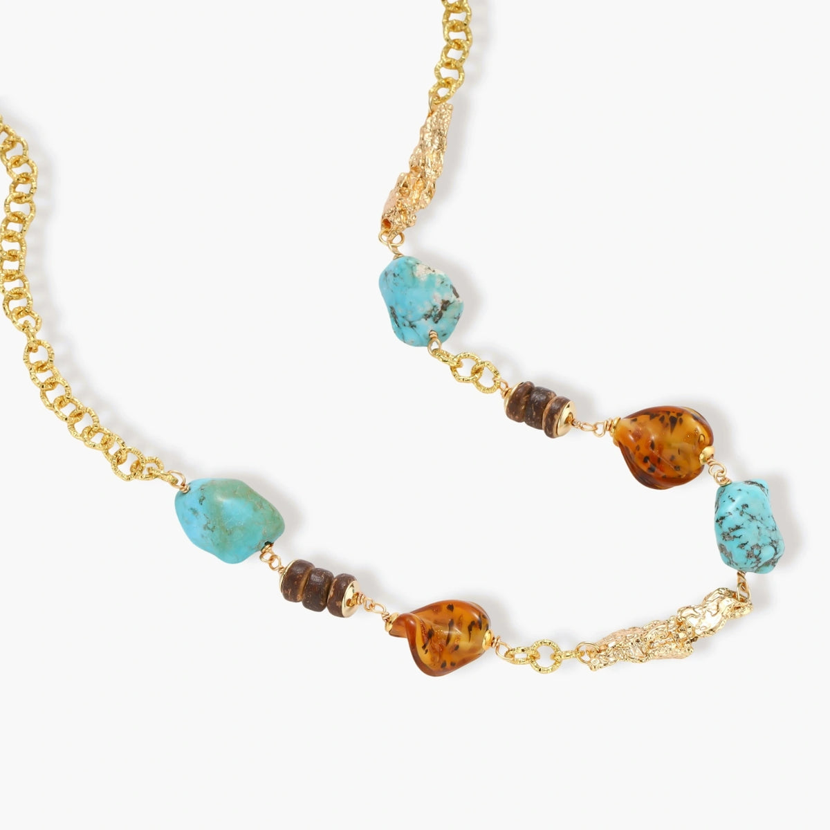 Gold plated eco-brass chain necklace with turquoise nuggets, amber-toned stones, brown discs and molten gold accents on cream.