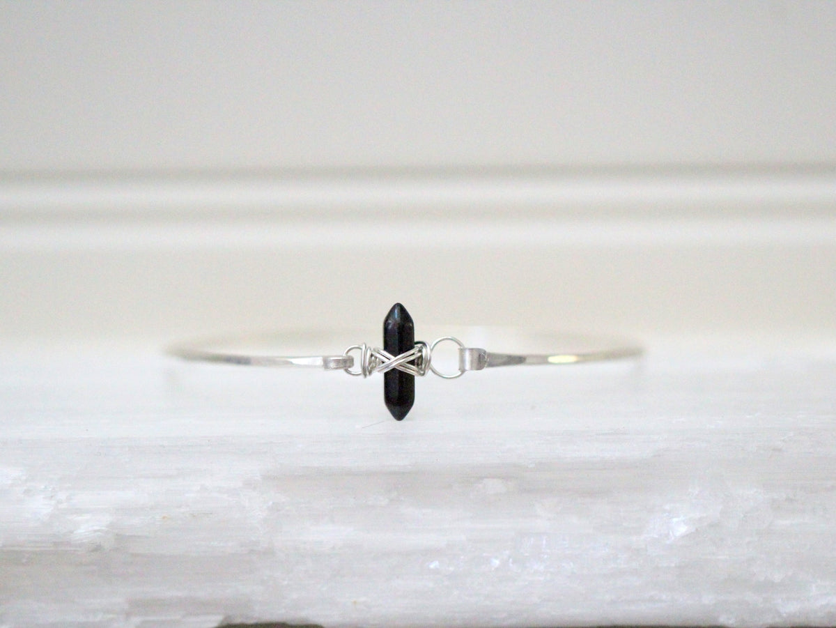 Obsidian crest bracelet flat lay, black beaded band with a crest charm for stacking
