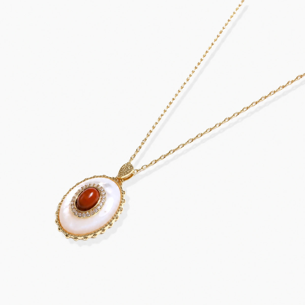 Gold plated eco-brass necklace with an oval white pendant, a central red-brown stone and a zirconia halo on a cream background.