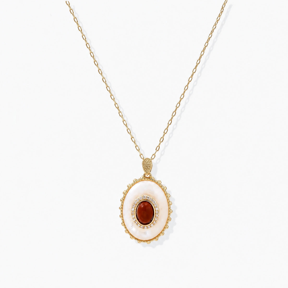 Gold plated eco-brass necklace with an oval white pendant, a central red-brown stone and a zirconia halo on a cream background.