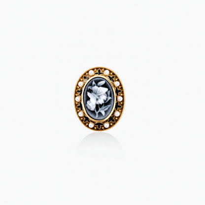 Gold-plated ring with oval blue floral cameo, pearl accents, and black enamel detailing on white background.