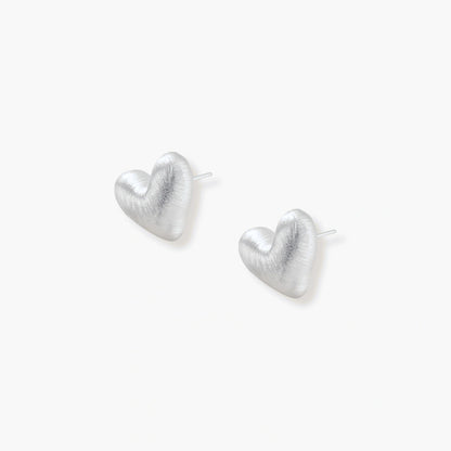 Pair of brushed platinum-plated 925 sterling silver puffy heart stud earrings on a cream background.