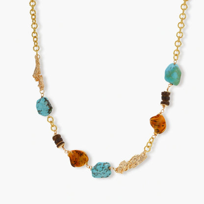 Gold plated eco-brass chain necklace with turquoise nuggets, amber-toned stones, brown discs and molten gold accents on cream.