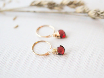 Close-up of garnet huggie hoop earrings, rich red dangle gemstones on a minimal hoop