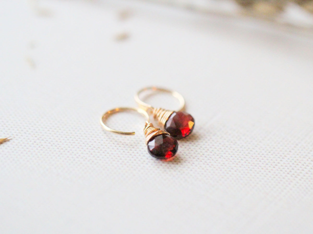 Garnet dangle huggie earrings worn on an ear, petite red gemstone hoops for stacking