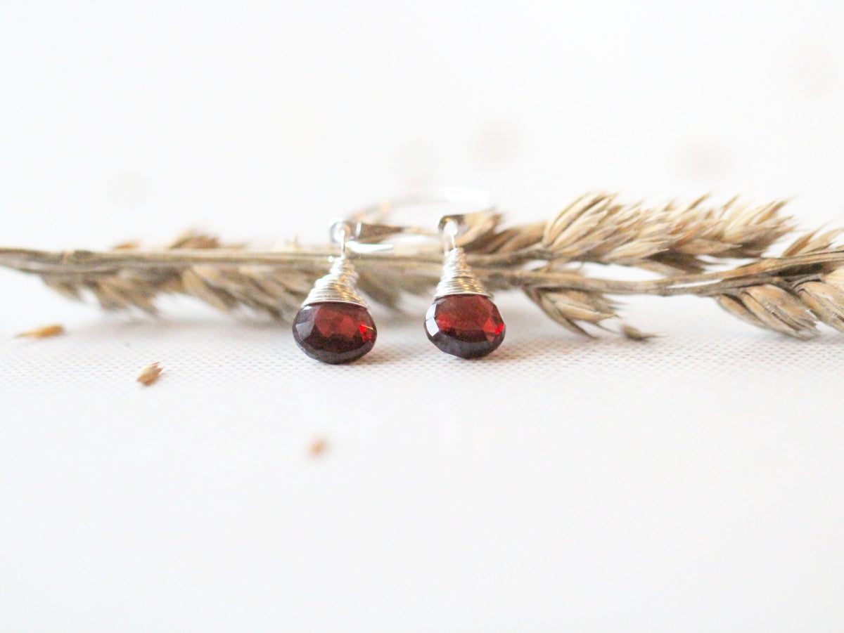Deep red garnet dangle huggie earrings flat lay, small hoops with faceted gemstone drops