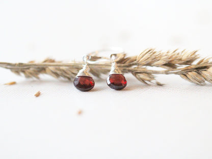 Deep red garnet dangle huggie earrings flat lay, small hoops with faceted gemstone drops