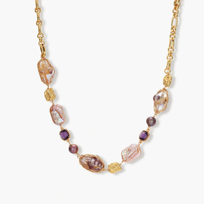 Gold plated chain necklace with wire-wrapped baroque pearls, purple faceted stones and textured gold beads on a cream background.
