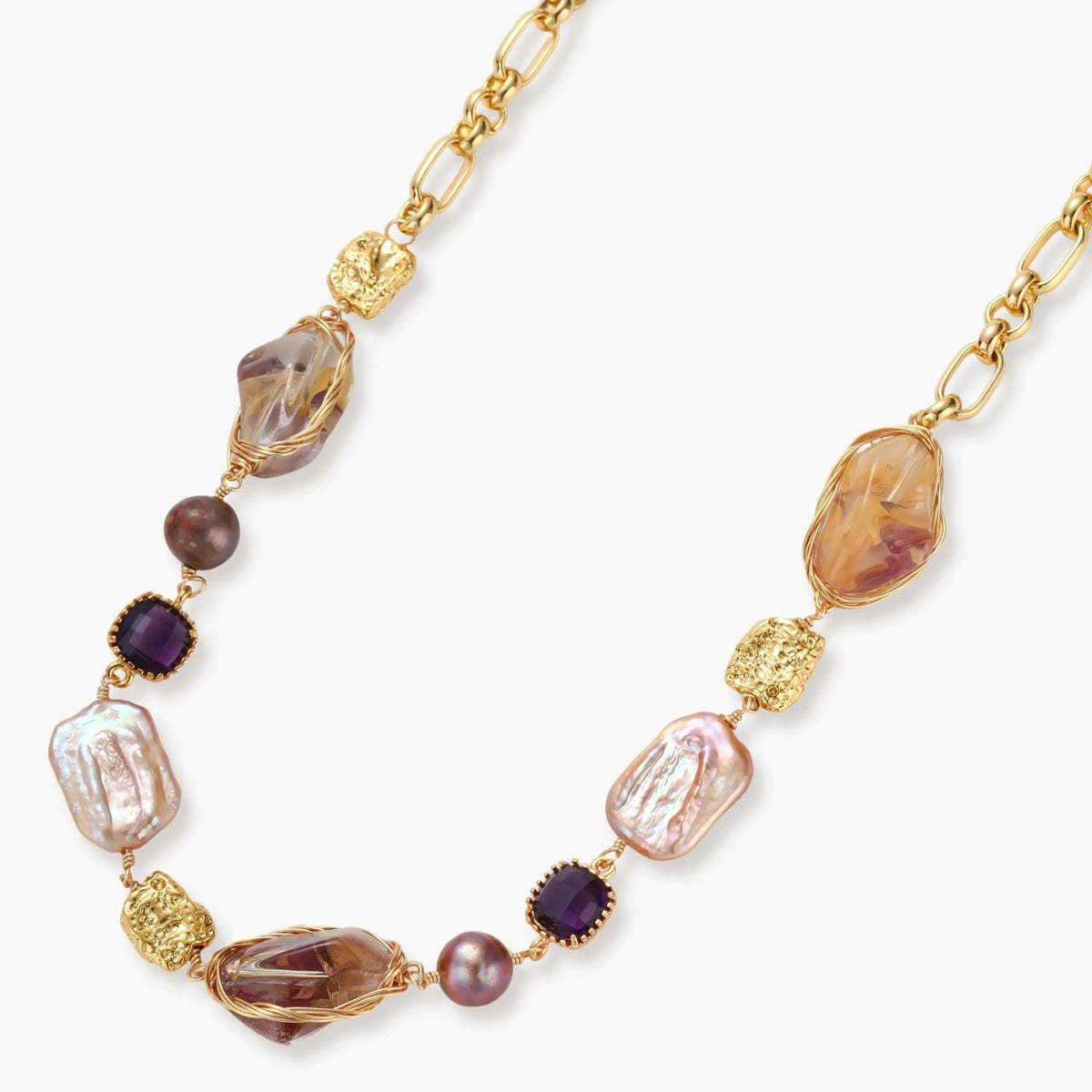Gold plated chain necklace with wire-wrapped baroque pearls, purple faceted stones and textured gold beads on a cream background.